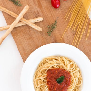 white ceramic bowl with pasta and red tomato on brown wooden table