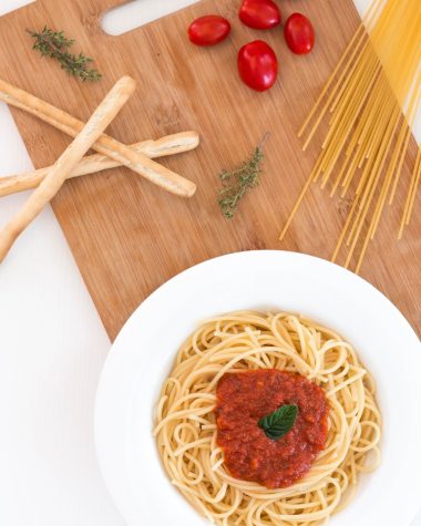 white ceramic bowl with pasta and red tomato on brown wooden table